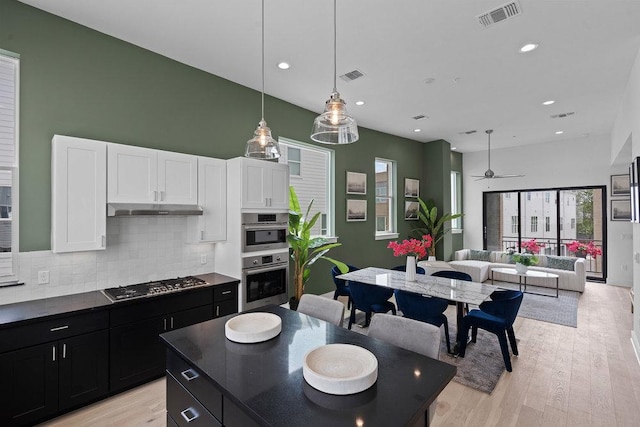 kitchen with dark cabinetry, stainless steel appliances, decorative backsplash, under cabinet range hood, and visible vents