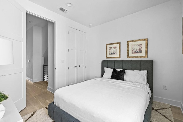 bedroom with baseboards, visible vents, wood finished floors, and a closet