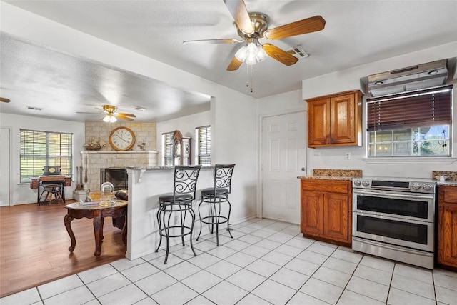 491 Herron Trl, Mcdade, TX 78650 - kitchen with range with two ovens, ceiling fan, a breakfast bar, brown cabinets, and a fireplace
