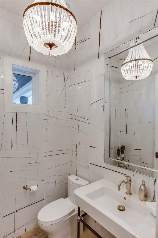 half bath with a sink, tile walls, toilet, and a chandelier