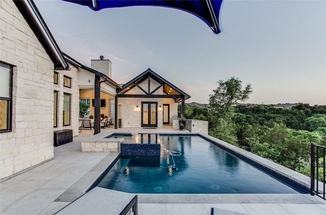 pool at dusk with an outdoor pool, french doors, a patio, and an in ground hot tub