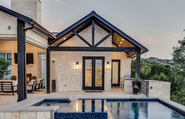 rear view of house with french doors, a patio area, an outdoor pool, and stone siding