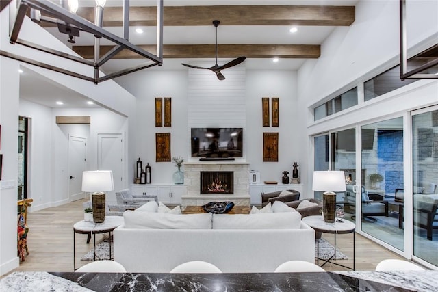 living room featuring beamed ceiling, a ceiling fan, wood finished floors, a stone fireplace, and a towering ceiling