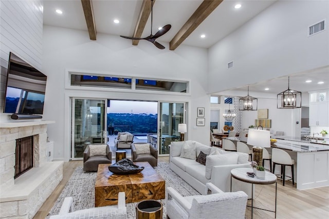 living area featuring visible vents, beamed ceiling, a stone fireplace, light wood-style floors, and a notable chandelier