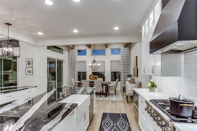 kitchen with light wood-style floors, white cabinetry, wall chimney exhaust hood, and an inviting chandelier