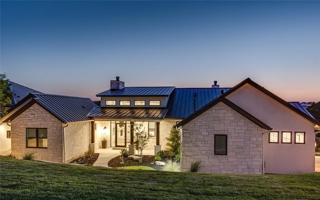 back of property featuring a yard, stone siding, metal roof, and a standing seam roof