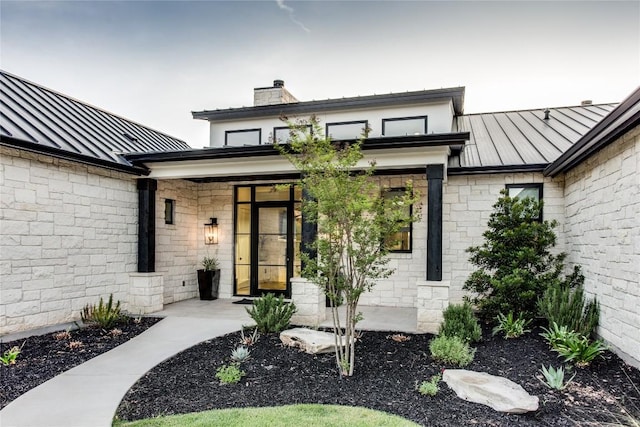 doorway to property featuring a standing seam roof, a chimney, and metal roof