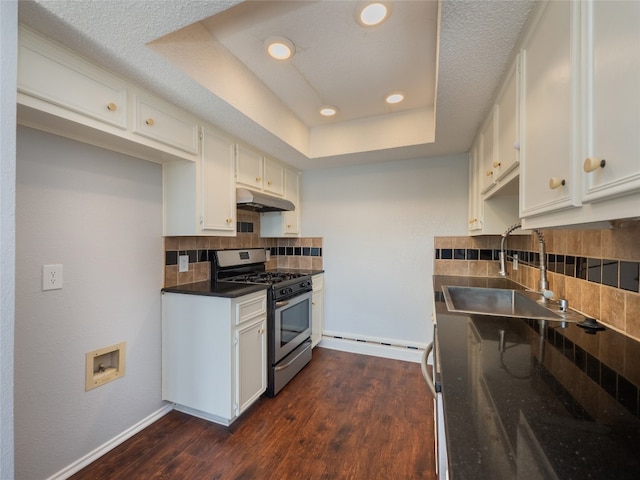 kitchen featuring a tray ceiling, a sink, dark wood-style floors, under cabinet range hood, and gas stove