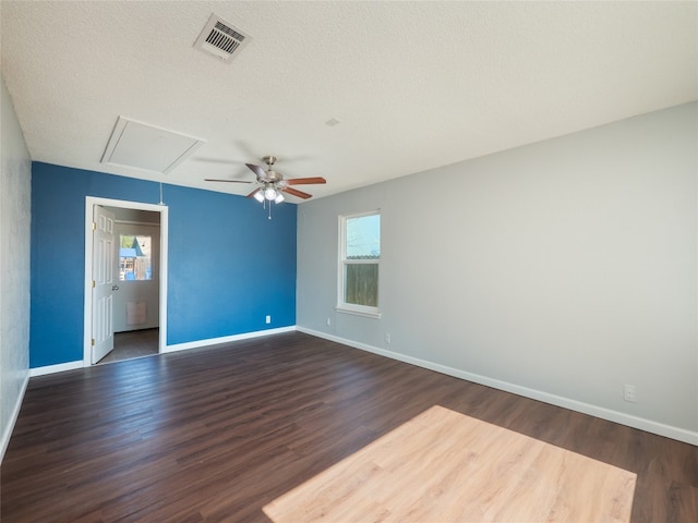 spare room featuring visible vents, baseboards, ceiling fan, attic access, and dark wood finished floors