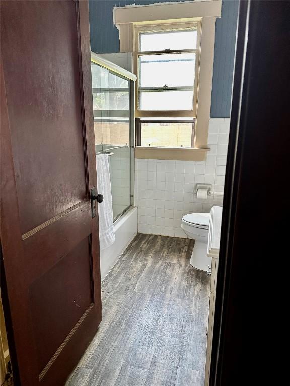 1106 Lexington St, Taylor, TX 76574 - full bathroom featuring toilet, tile walls, combined bath / shower with glass door, and wood finished floors