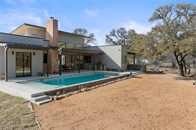 back of property with a patio area, a chimney, an outdoor pool, and stucco siding