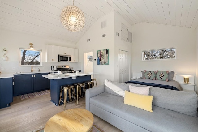 living room with light wood-type flooring, an inviting chandelier, visible vents, and high vaulted ceiling
