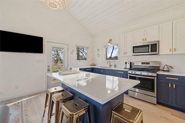 kitchen featuring stainless steel appliances, vaulted ceiling, a kitchen bar, light wood-style floors, and light countertops