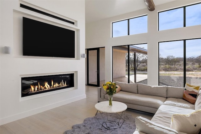 living area with a glass covered fireplace, baseboards, wood finished floors, and a towering ceiling