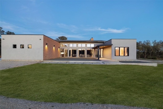 rear view of house featuring a patio area, a yard, and stucco siding