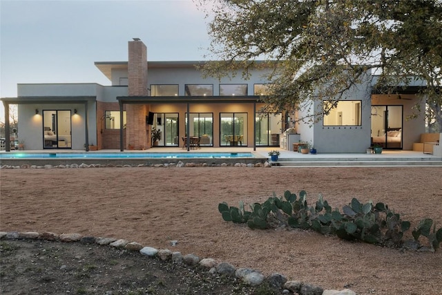 rear view of house featuring stucco siding, an outdoor pool, a chimney, and a patio