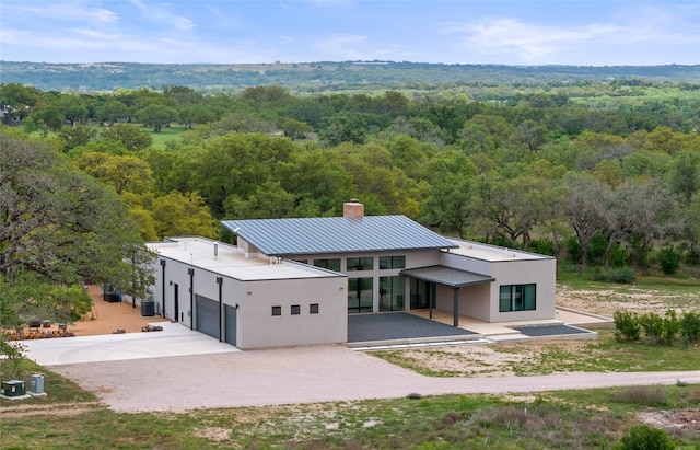 back of property featuring driveway, metal roof, a wooded view, and stucco siding