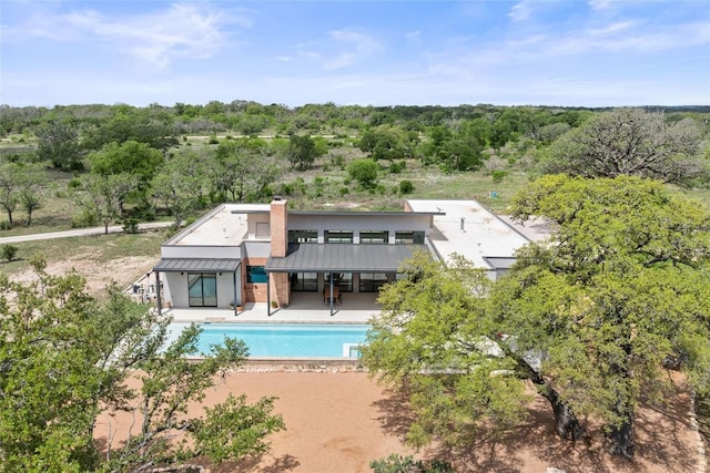 back of house featuring a standing seam roof, a chimney, metal roof, a patio, and an outdoor pool