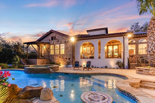 3312 Pearce Rd, Austin, TX 78730 - back of house with a tile roof, stone siding, solar panels, a pool with connected hot tub, and stucco siding