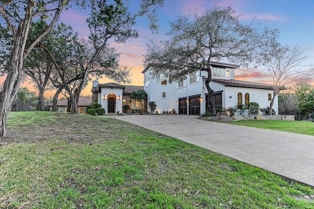 mediterranean / spanish-style house featuring a garage, stucco siding, a tiled roof, and a front lawn