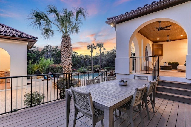 deck at dusk featuring an outdoor pool, outdoor dining area, and a ceiling fan