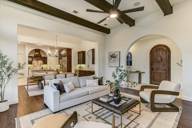 living area featuring visible vents, ceiling fan with notable chandelier, arched walkways, and dark wood-style flooring