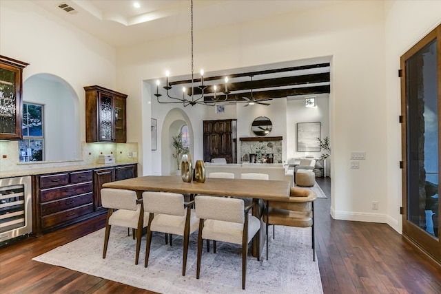 dining area with visible vents, beverage cooler, ceiling fan with notable chandelier, arched walkways, and dark wood-style flooring