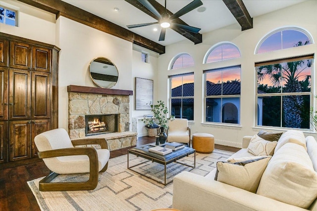 living area featuring a stone fireplace, beam ceiling, wood finished floors, and ceiling fan