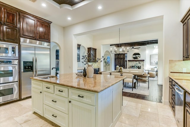 kitchen featuring light stone counters, a sink, recessed lighting, arched walkways, and built in appliances
