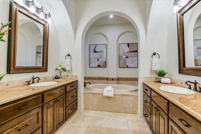 full bath with tile patterned floors, two vanities, a bath, and a sink
