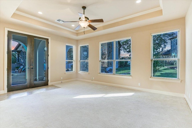carpeted spare room featuring a tray ceiling, french doors, visible vents, and ornamental molding