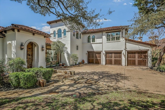 mediterranean / spanish house with stucco siding, driveway, a tile roof, and a garage