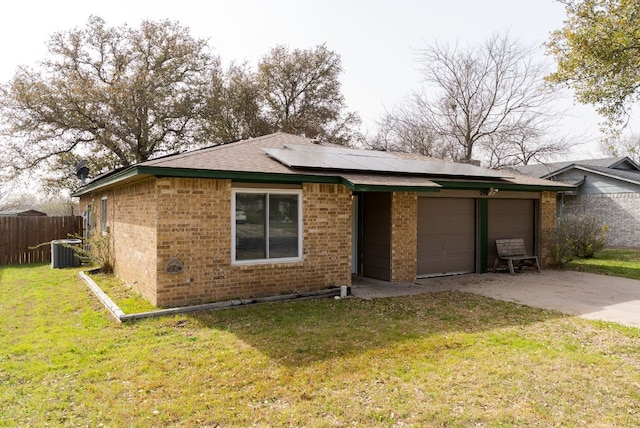 view of front facade featuring driveway, roof mounted solar panels, fence, a front yard, and brick siding