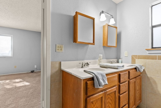 bathroom with a sink, a textured ceiling, double vanity, and a textured wall