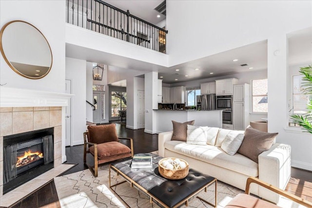 living room with light wood finished floors, a tiled fireplace, baseboards, and a high ceiling