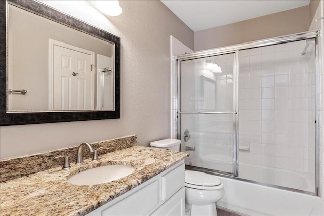 full bath with toilet, vanity, combined bath / shower with glass door, and a textured wall