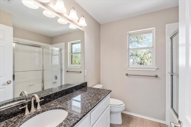 bathroom with a shower with shower door, baseboards, toilet, vanity, and wood finished floors
