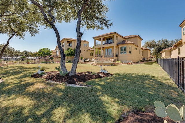 back of house with a fenced backyard, a tiled roof, a lawn, and a balcony