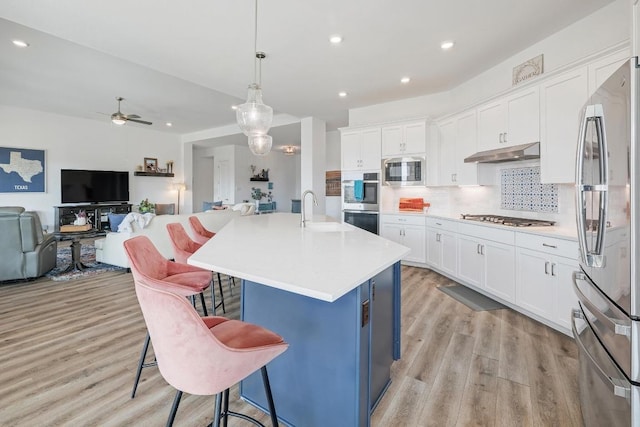 kitchen featuring under cabinet range hood, a sink, a kitchen breakfast bar, backsplash, and stainless steel appliances