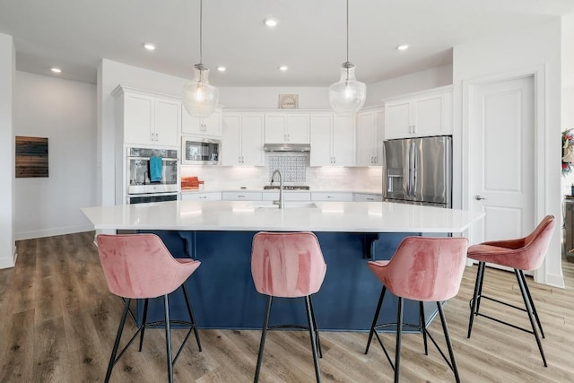 kitchen with a sink, white cabinetry, stainless steel appliances, light wood-style floors, and decorative backsplash