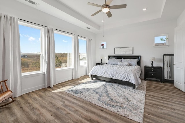 bedroom featuring a raised ceiling, wood finished floors, visible vents, and baseboards