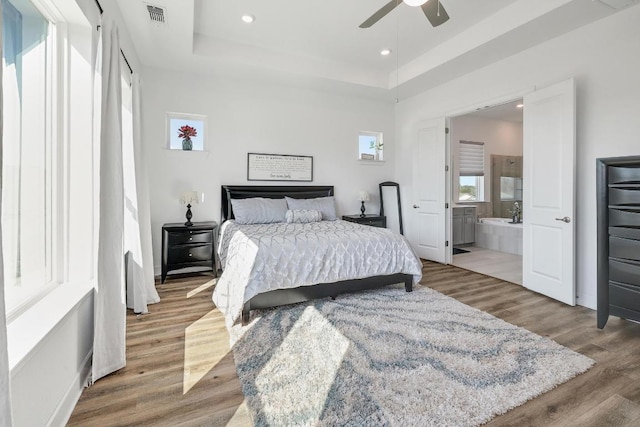 bedroom with visible vents, a tray ceiling, ensuite bath, wood finished floors, and recessed lighting