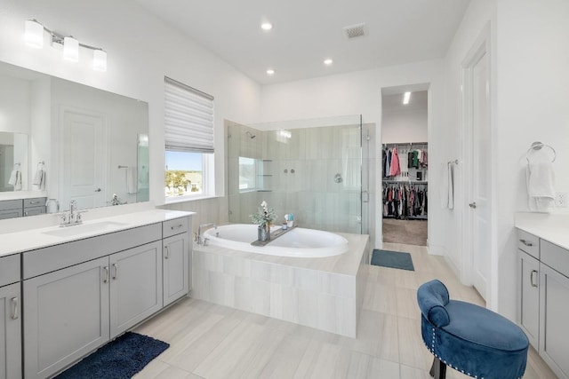 full bathroom with a spacious closet, visible vents, a garden tub, a stall shower, and a sink