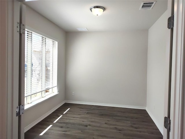 spare room with dark wood-type flooring, baseboards, visible vents, and a wealth of natural light