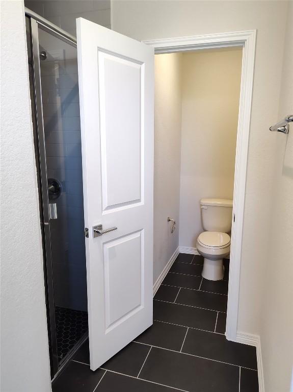 bathroom with tile patterned floors, baseboards, toilet, and a stall shower