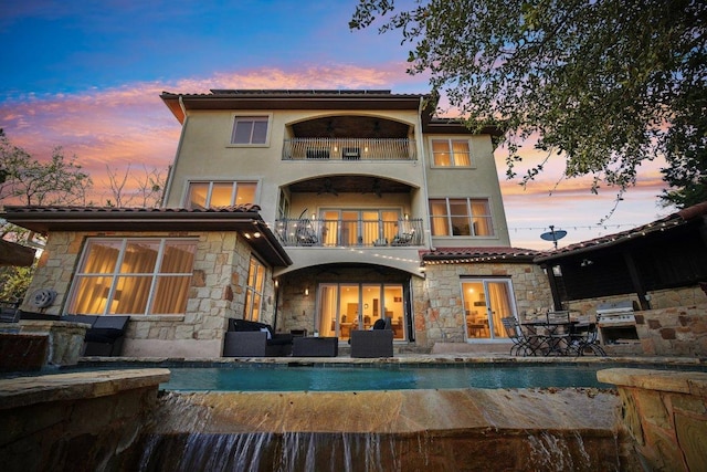 23617 Indian Divide Cv, Spicewood, TX 78669 - back of property featuring a balcony, an outdoor hangout area, stone siding, and an outdoor pool