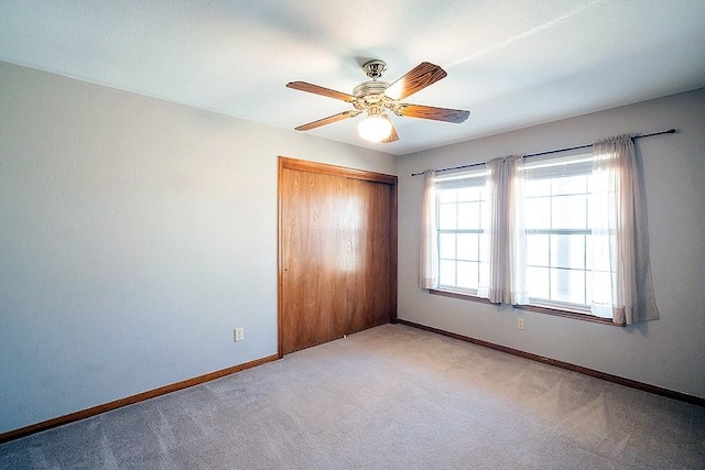 unfurnished bedroom with a closet, light colored carpet, a ceiling fan, and baseboards