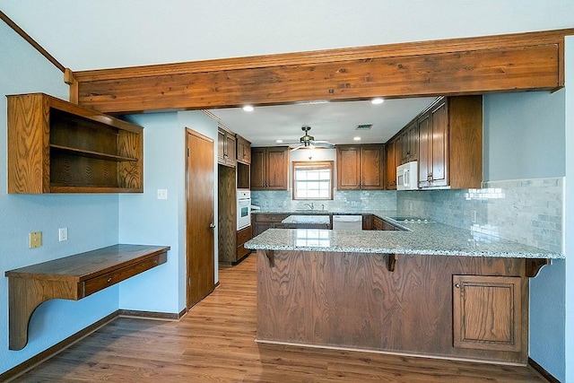kitchen with a sink, wood finished floors, white appliances, a peninsula, and light stone countertops