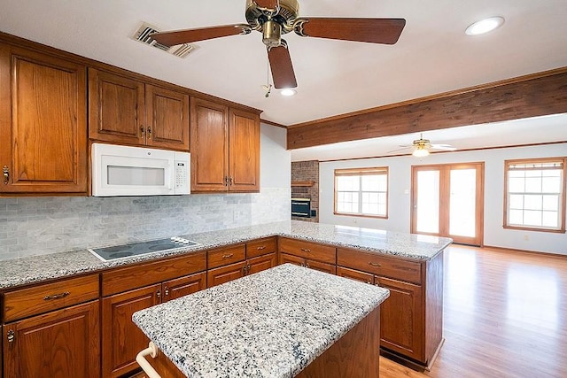 kitchen with white microwave, visible vents, a peninsula, ceiling fan, and black electric stovetop