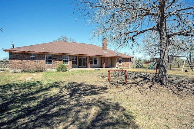 back of house featuring fence, a chimney, a playground, a lawn, and brick siding